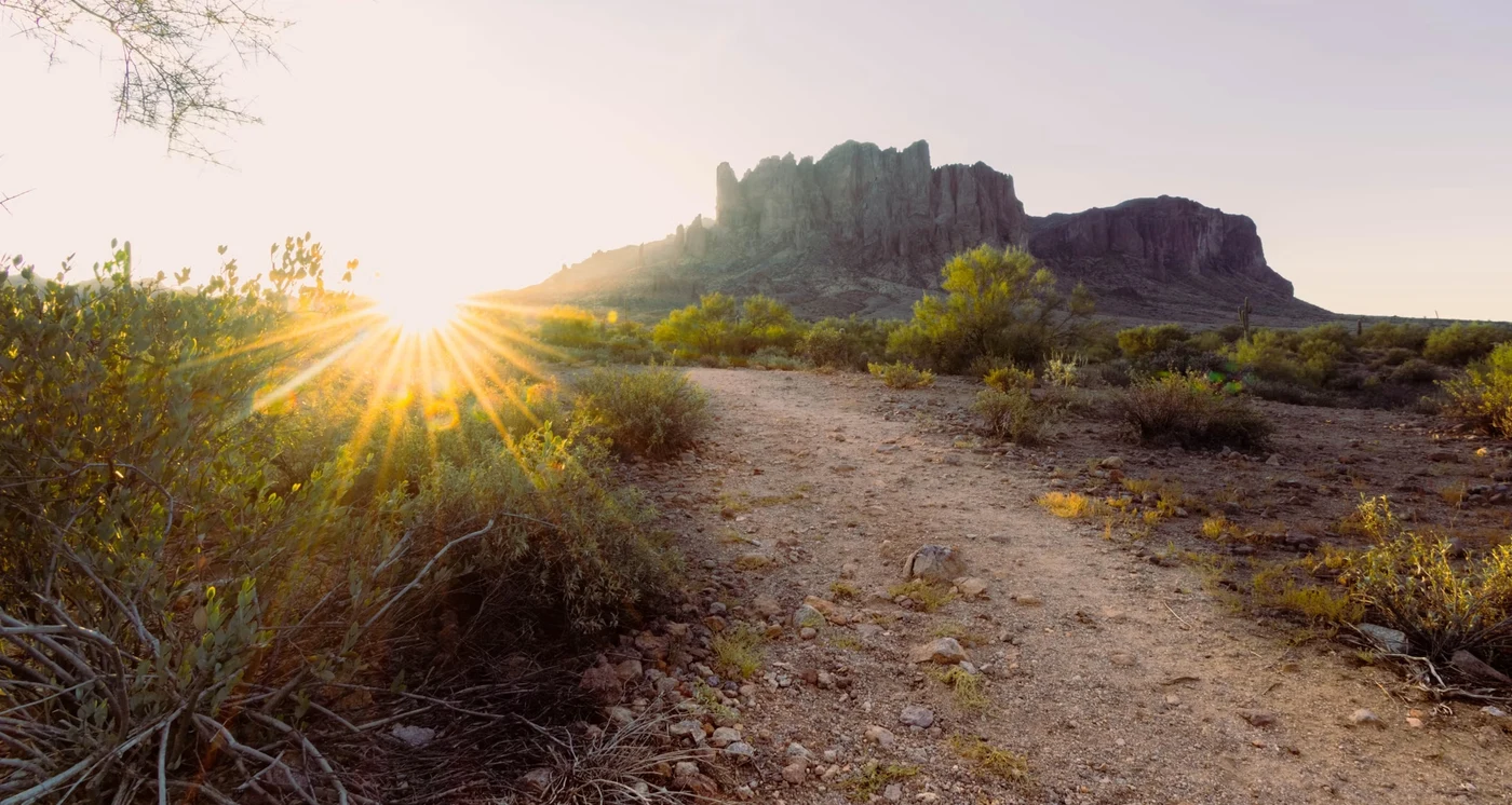 A dirt path leading toward the Flatiron rock formation at sunrise in the Arizona desert, different starting points leading to the same place.